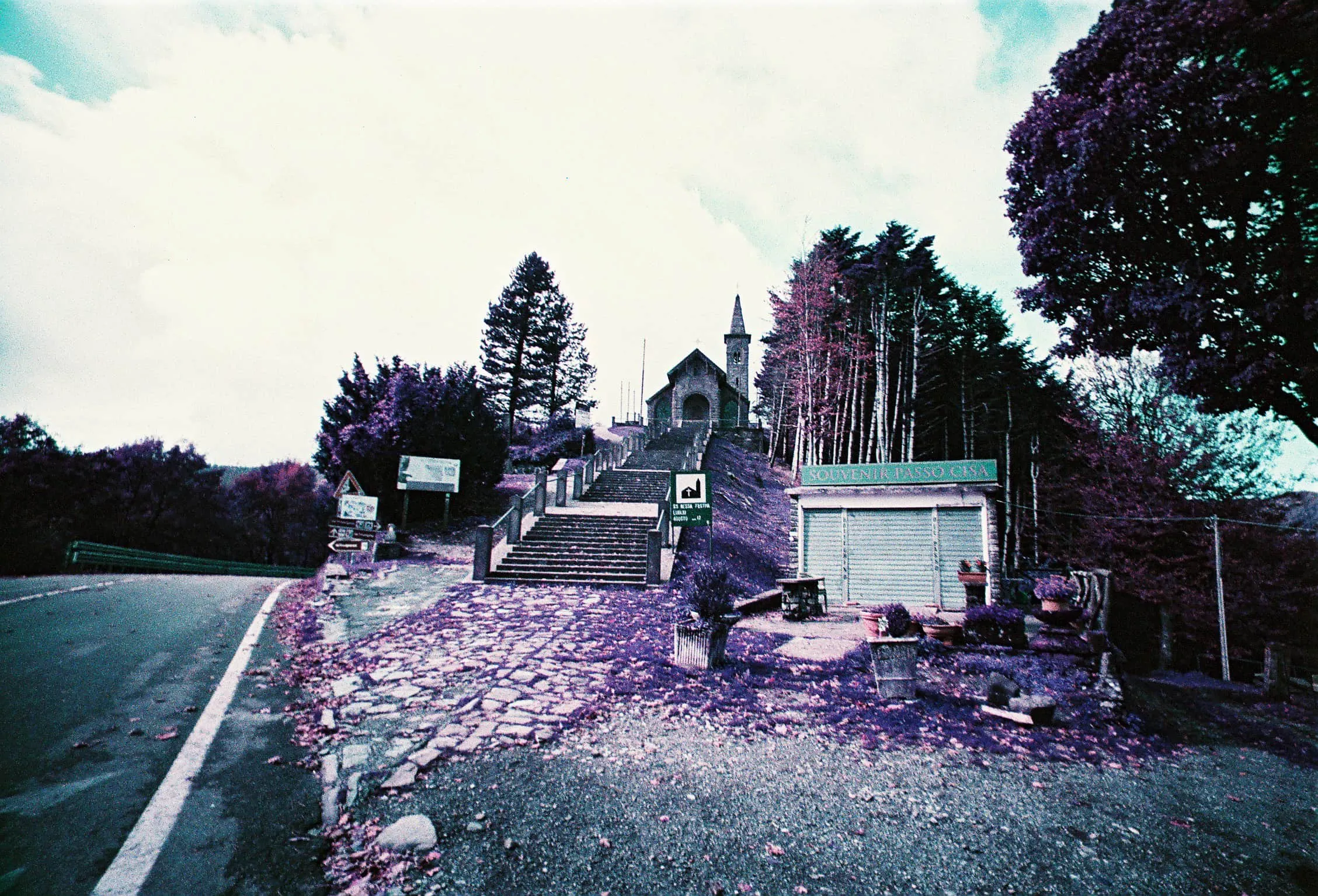 Lomo Purple film photograph of a road and stone path leading to a small church or chapel in the hills.