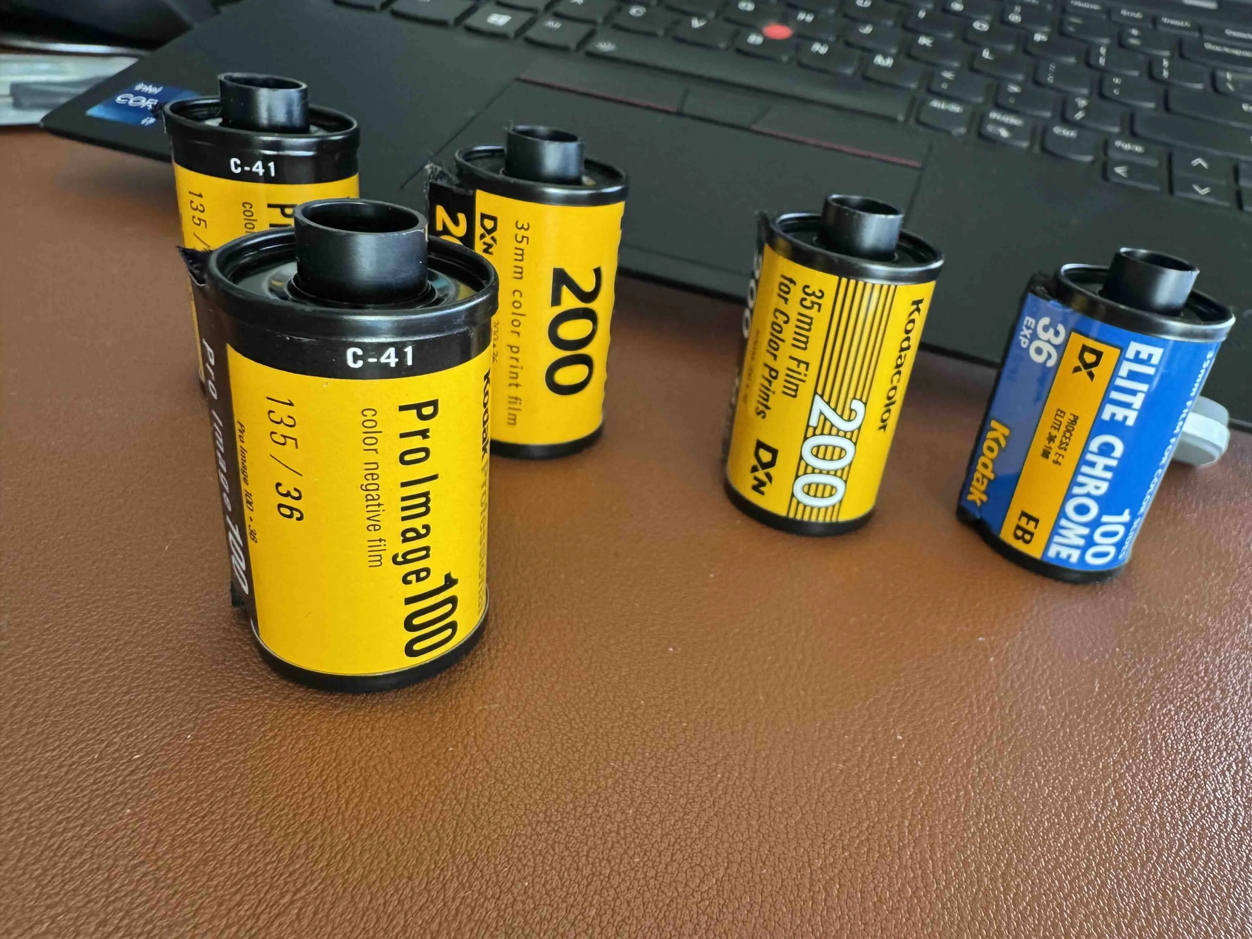 Several undeveloped 35mm kodak film rolls on a desk beside a laptop